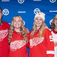 Group of 4 with Red Wings jerseys on standing in front of GVSU backdrop